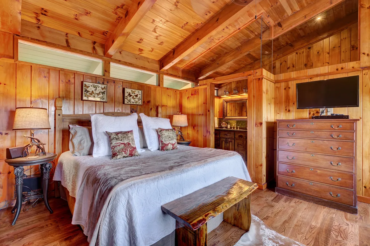A luxurious master suite with a king-sized bed, decorative pillows, wooden accents, and a peaceful, light-filled ambiance. The room includes thoughtful touches for comfort and relaxation, suggesting an adjoining en-suite bath and workspace.
