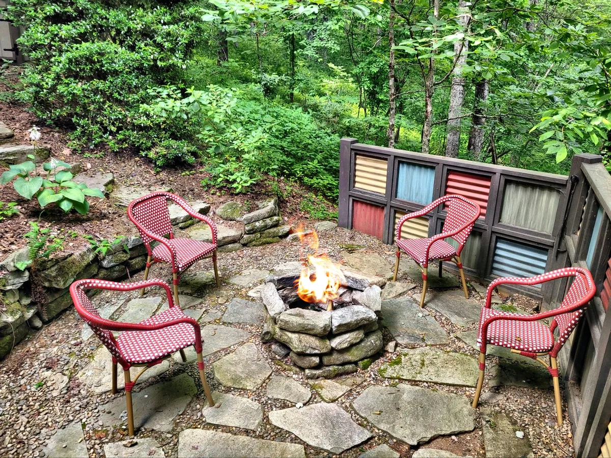 This image captures a fire pit surrounded by vibrant red chairs on a terrace with wooden paneling. The setting is framed by natural greenery, inviting guests to gather, relax, and enjoy the warmth of the fire under the open sky.