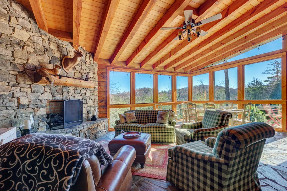 A comfortable seating area featuring plaid armchairs, a substantial stone fireplace, and expansive windows that invite in natural light and panoramic mountain vistas. The arrangement exudes warmth and encourages relaxation, reading, or socializing while enjoying the outdoors from within.