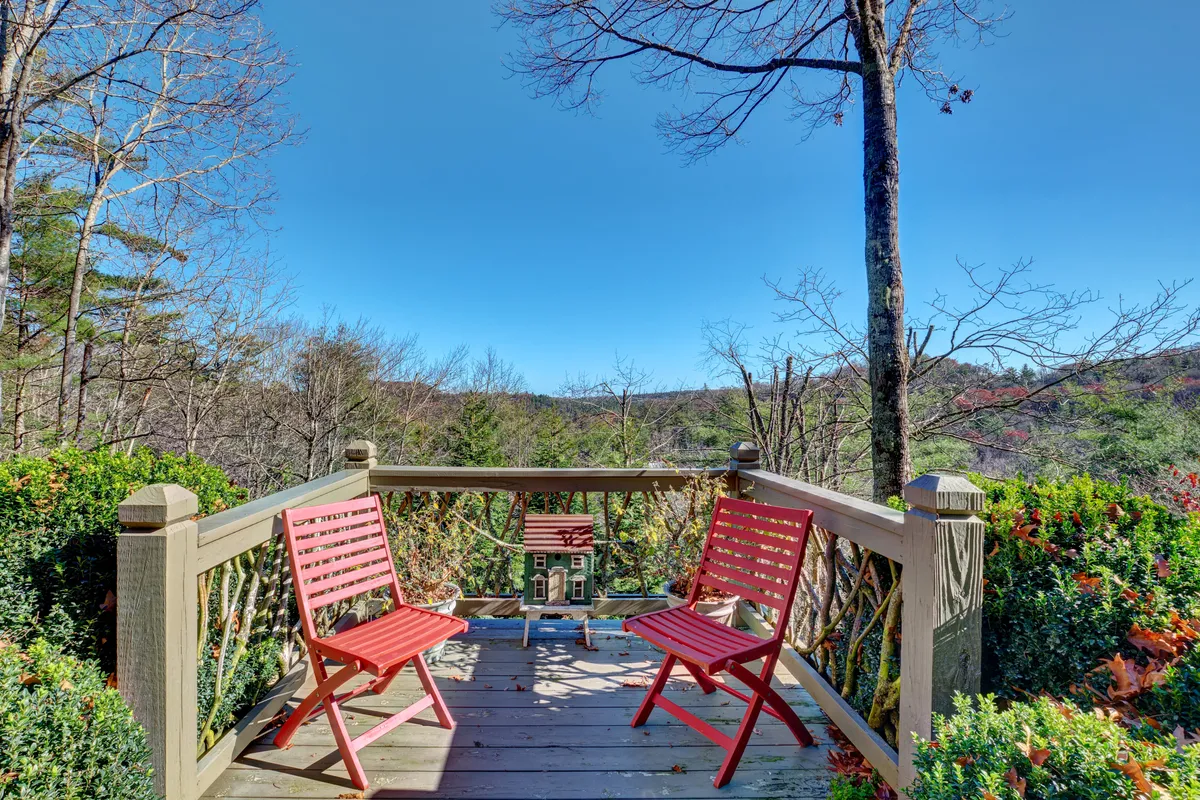 A scenic exterior view featuring a pair of red chairs positioned to take in the tranquil mountain scenery, with the decorative house and surrounding trees providing a sense of peaceful seclusion.